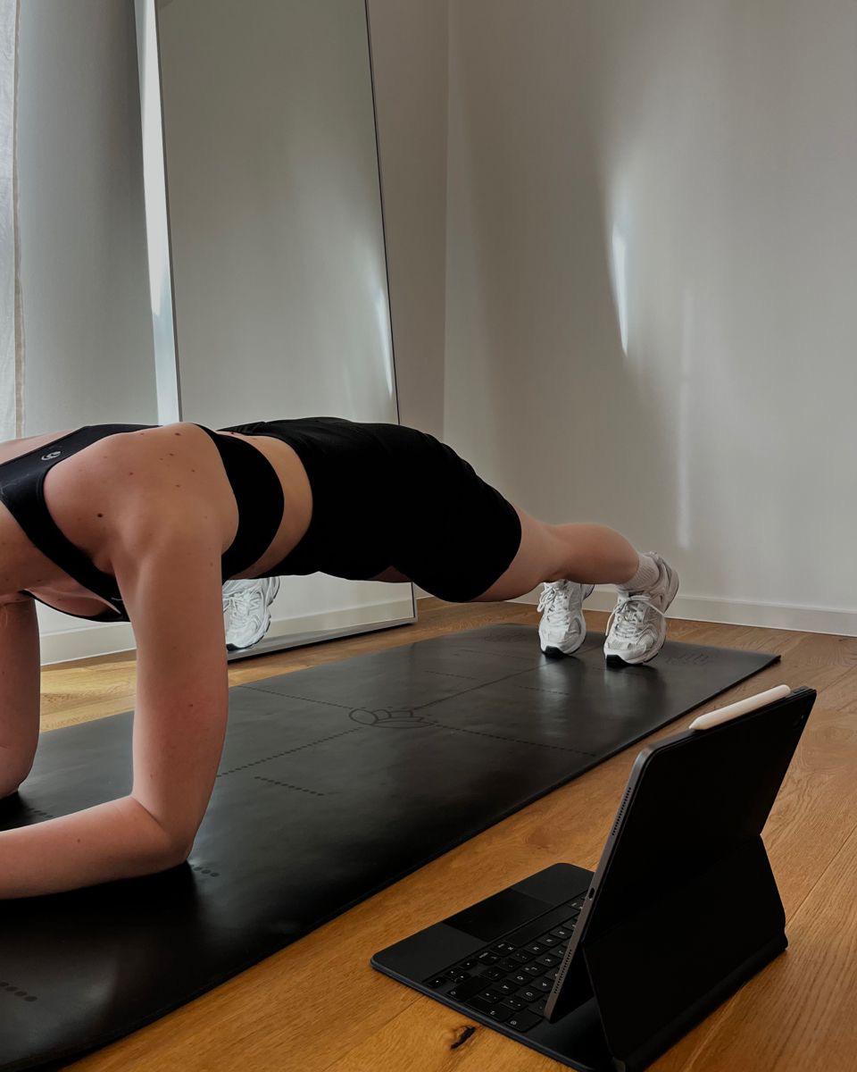 Atleta in plank su tappetino durante una sessione di allenamento online via tablet
